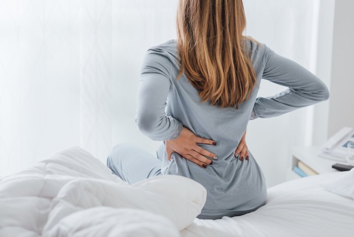 Woman with aching back getting up from bed.