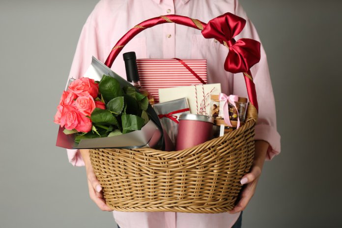 Woman holding wicker basket full of presents on grey background closeup