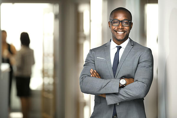 African American executive in a gray suit stands smiling with his arms crossed