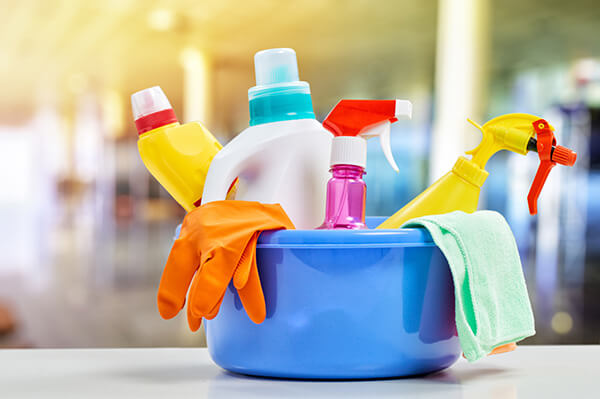 Basket with cleaning items on blurry background, illustration for COVID-19 hygiene