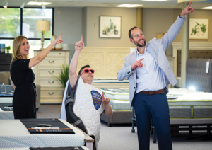 LOOK, UP IN THE SKY It’s a bird! It’s a plane! No, it’s Mattman. Sweet Dreams Mattress & Furniture owners Katy Law (left) and Greg Law (right) pose with Mattman (aka store manager Andrew Schlesser) at their store in Cornelius, North Carolina.