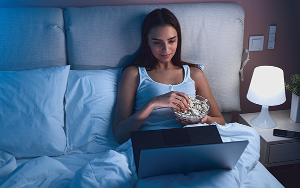 woman sitting in bed eating popcorn and watching a show on her laptop