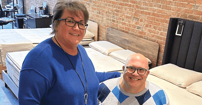 IN SYNC Sandman Sleep co-owners Kim and Rich Hanschu pose on an Avocado Green Mattress inside the showroom.