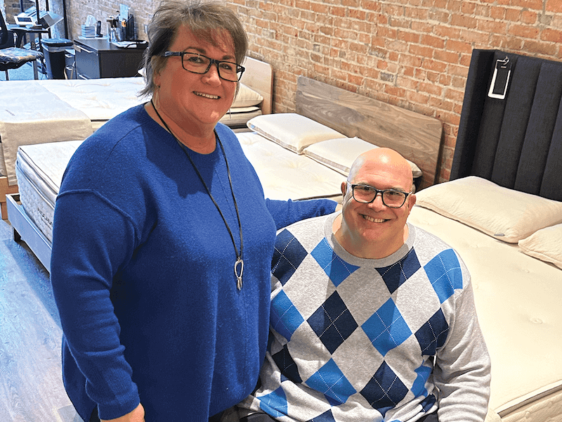 IN SYNC Sandman Sleep co-owners Kim and Rich Hanschu pose on an Avocado Green Mattress inside the showroom.